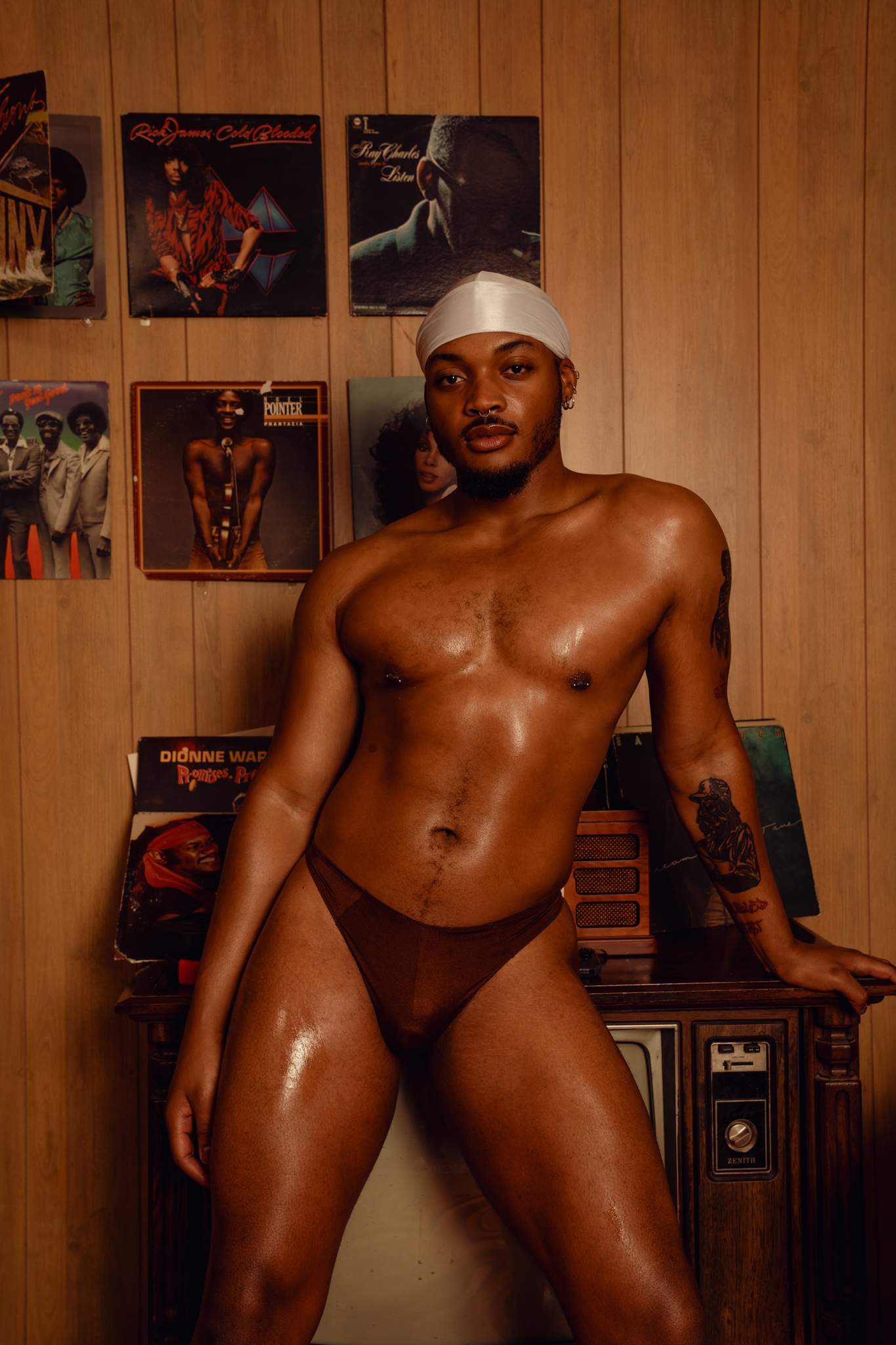 Man posing in a room with vinyl records on the wall in an Akate classic brown nylon thong