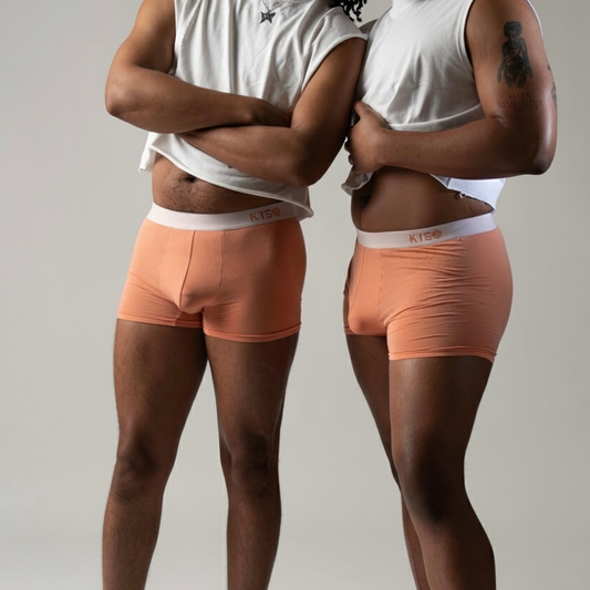 Two people wearing peach boxer briefs with white waistbands on a neutral background